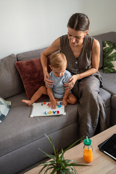 Mother helping toddler son learn letters on sofa at home