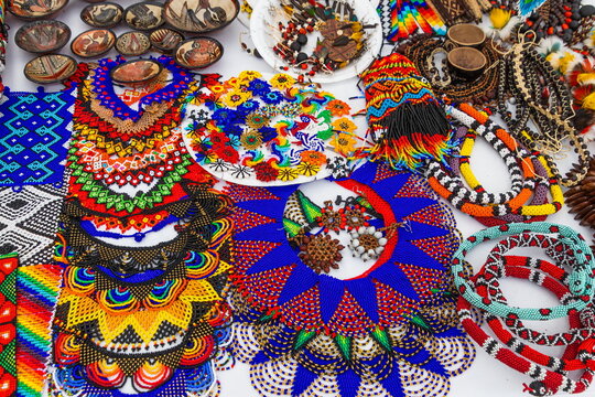 Vibrant handcrafted traditional Andean Kichwa-style beaded jewelry, including colorful traditional beads, round necklaces, and braided bracelets, are displayed at an open-air market in Cuenca, Ecuador