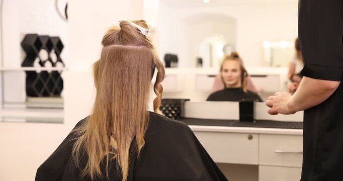 Hairdresser styling woman's hair with curling iron in beauty salon, closeup