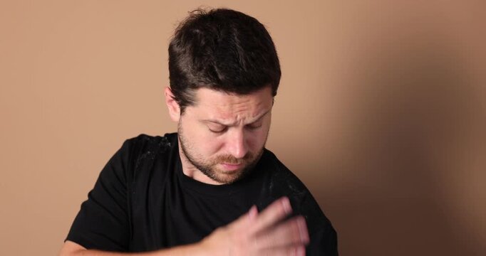 Worried man brushing dandruff off his t-shirt on beige background. Camera moving forward