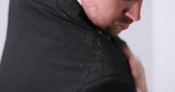 Man brushing dandruff off his suit on blurred grey background. Camera moving forward