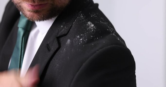Man brushing dandruff off his suit on blurred grey background, closeup. Camera moving forward and backwards