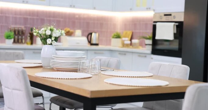 Stylish setting with vase of flowers, plates and glasses on wooden table in kitchen. Camera moving