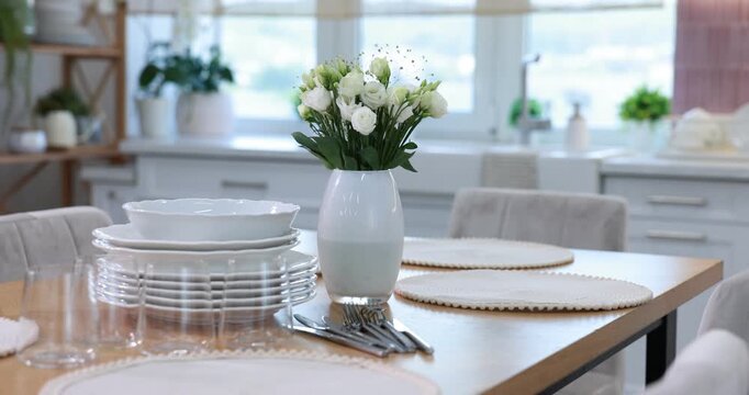 Stylish setting with vase of flowers, plates and glasses on wooden table in kitchen. Camera spinning