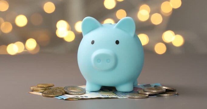 Woman putting coins into piggy bank against grey background with blurred lights, closeup. Bokeh effect