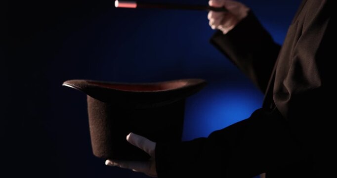 Magician showing trick with wand and top hat on stage, closeup