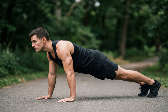 Fit man performing pushups outdoors in park environment