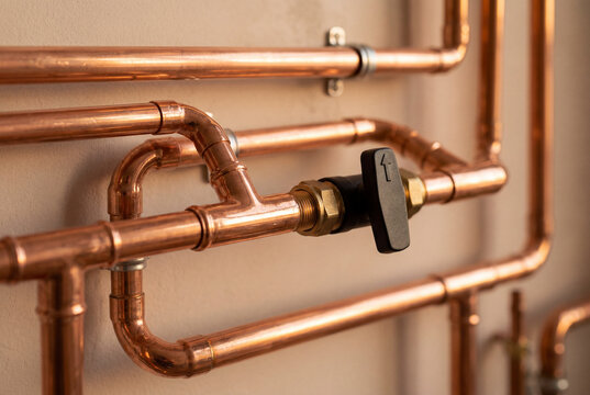 Copper heating pipes with a black shut off valve installed against a wall