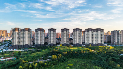 Fototapeta premium Modern high-rise residential buildings stand adjacent to a lush green urban landscape under a clear blue sky.