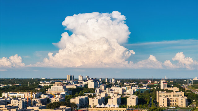A panoramic urban landscape showing various buildings under a vivid blue sky with a large fluffy cumulus cloud above the city.