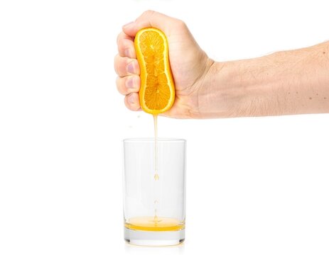 Close-up of one adult hand squeezing a halved orange into a clear glass, with fresh juice dripping against a clean white background and ample copy space.