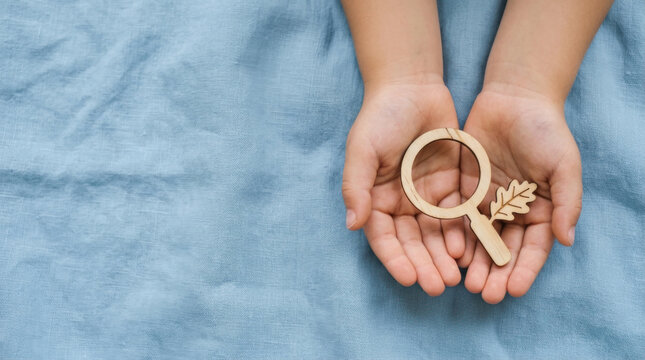 Child hands holding a wooden magnifying glass with a leaf icon representing nature exploration, environmental education, and outdoor childhood discovery.