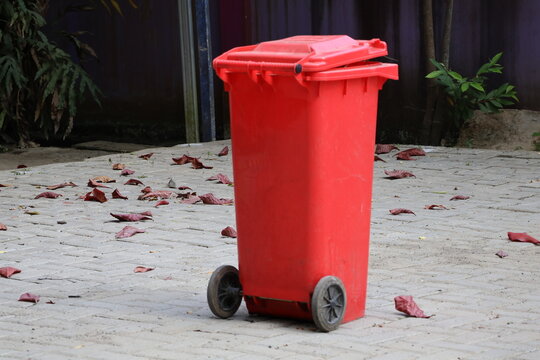 Trash bin surrounded by scattered fallen leaves in outdoor environment naturally