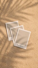 Fototapeta premium Blank instant photo prints on sandy background with palm leaf shadows.