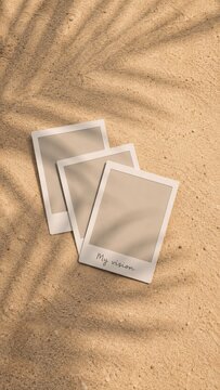 Blank instant photo prints on sandy background with palm leaf shadows.
