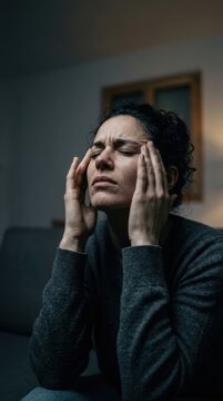Woman Experiencing Migraine Headache And Stress Sitting In A Dark Room