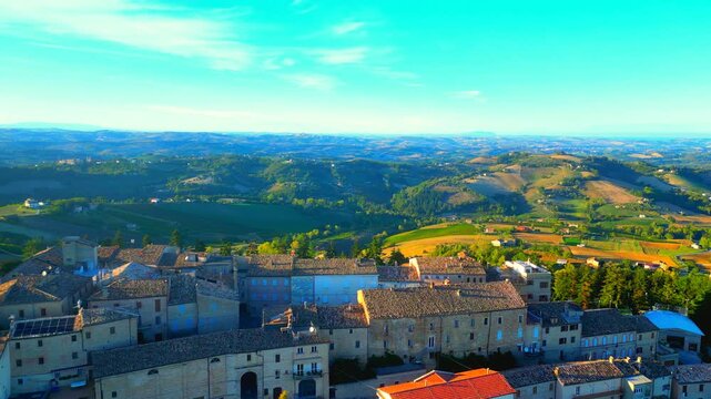 Interesting aerial truck left shot from Monte Rinaldo, capturing the town's inner square delimited by buildings, walls and arches, surrounded by precious Marche hillscapes, Mount Conero, sea, hazy sky