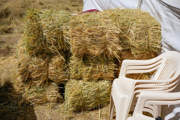 Dry hay bales stacked next to white plastic chairs for cattle feed © WILL PHOTOGRAPHY