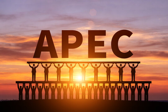 Numerous small figures silhouetted in the morning sun, holding up APEC