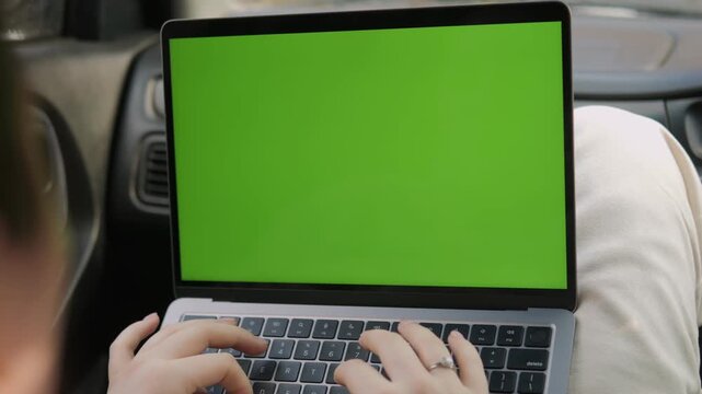 Person typing on laptop with green screen in car. Hands move steadily over keyboard. Focus stays on screen for easy content replacement. Ideal for remote work, online meetings