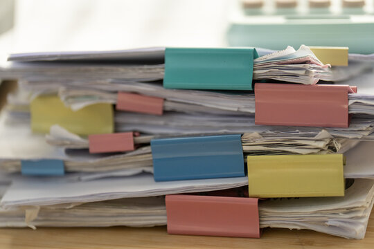 Stacks of papers bound with colorful tabs. Office clutter signals busy workdays. Colorful tabs add visual order to chaos. Tired but productive workspace moment. Perfect for business, school