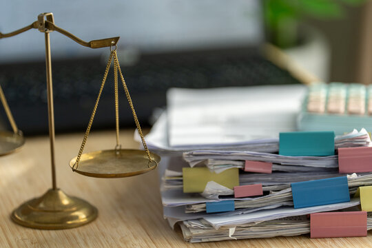 Golden scales sit beside stacks of papers with colorful tabs. Documents suggest legal or financial matters require careful judgment. The scene evokes balance, decision-making, and responsibility