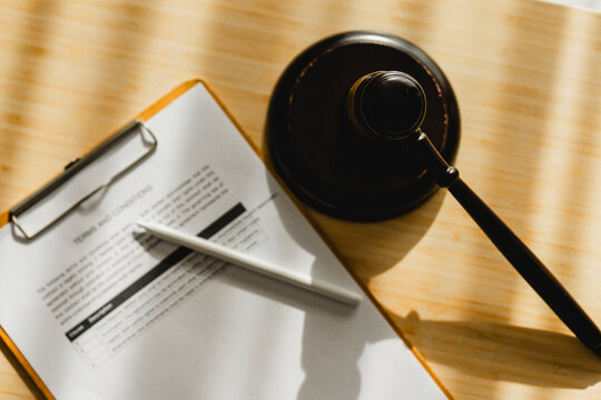 Gavel rests beside a clipboard and pen. Sunlight casts warm shadows across the surface. Documents imply legal or contractual matters. Scene suggests decision-making or finalization