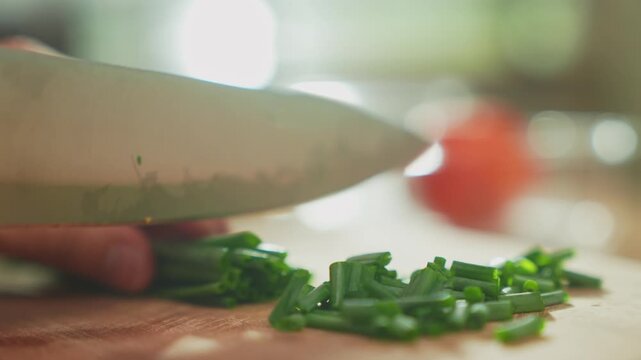 Woman&rsquo;s hand chopping green onion with kitchen knife on wooden cutting board