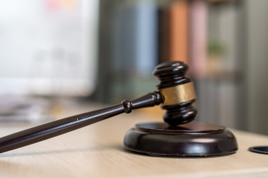 Wooden gavel rests on polished base. Blurred background hints at courtroom setting. Dark tones convey formality and authority. Gavel symbolizes justice, decisions, and legal proceedings