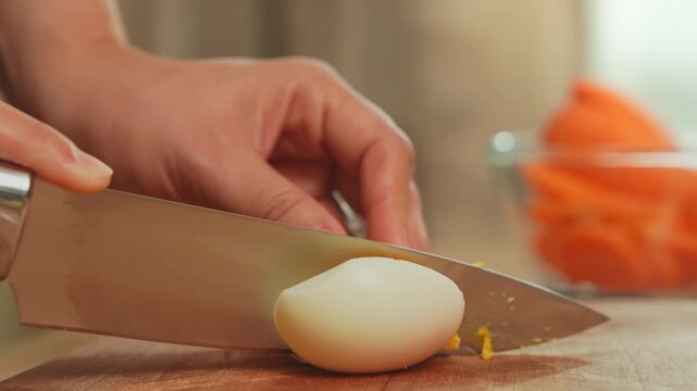 Close-up of woman hands cleanly slicing a boiled egg on a wood cutting board.
