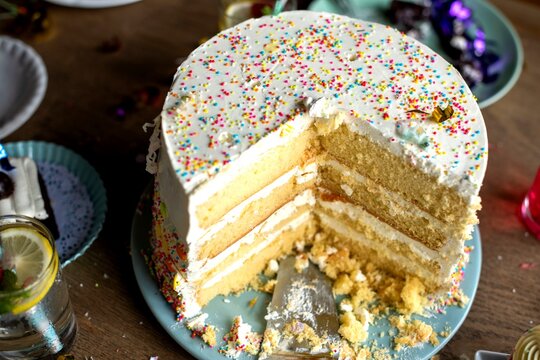 A sliced vanilla layer cake with sprinkles on a wooden table.