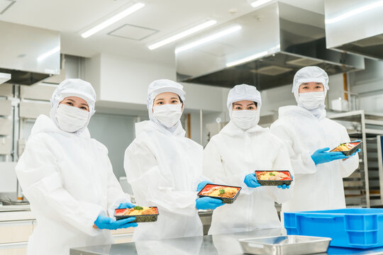 A man and a woman preparing bento boxes in a kitchen (food factory, food processing, food hygiene)