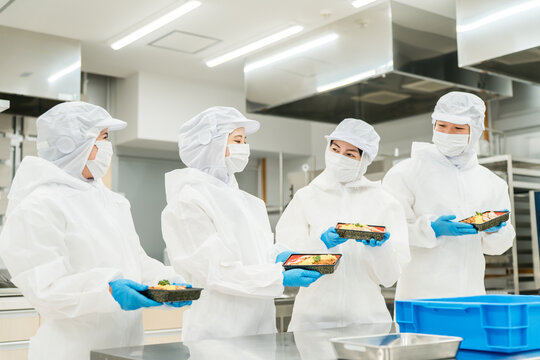 A man and a woman preparing bento boxes in a kitchen (food factory, food processing, food hygiene)