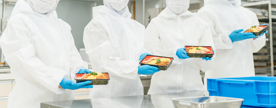 A man and a woman preparing bento boxes in a kitchen (food factory, food processing, food hygiene)