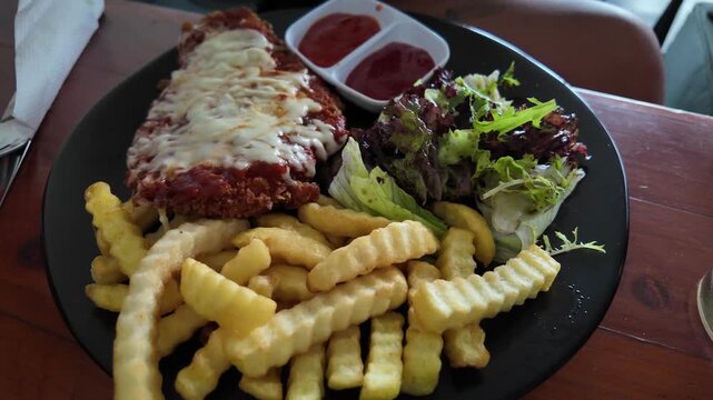 Chicken parmigiana with melted cheese and crinkle-cut fries on a plate