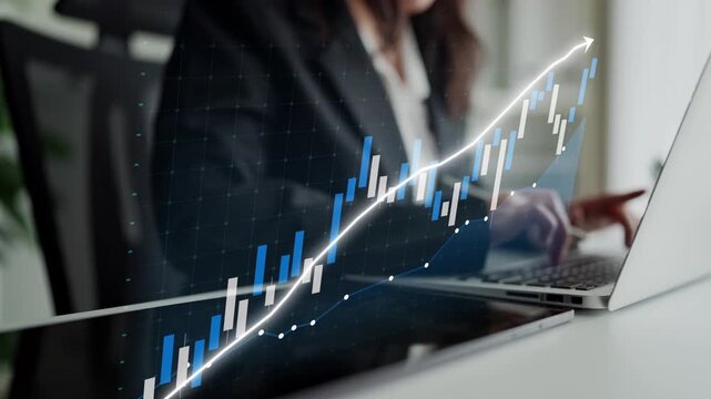 A business professional is focused on analyzing financial growth using a laptop and a digital graph, showcasing trends and market performance in a modern workspace. Copula