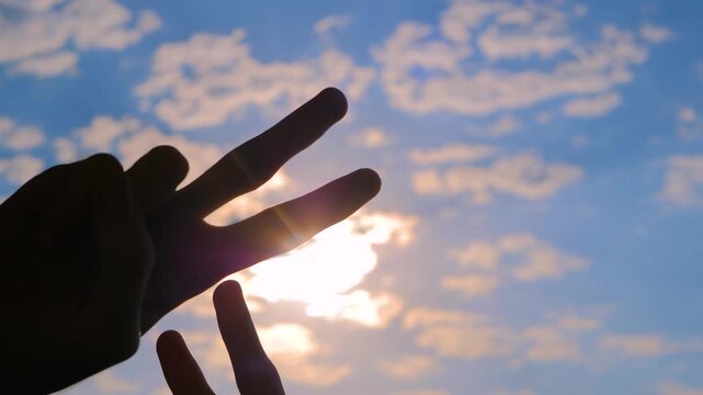 Silhouettes of four hands are showing victory sign, gesture of peace against the sunset or sunrise sky - close up view, sun lens flare. Friendship, unity, harmony and positive concept