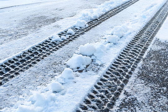 Tire tracks pressed into snow on a paved winter road, showing vehicle movement marks and compacted snow.