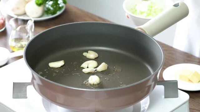 Finely chopped onions are added to a hot nonstick pan with garlic and olive oil, creating the aromatic foundation for a delicious homemade meal. Close-up cooking process in a bright modern kitchen,
