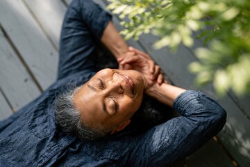 Obraz premium Serene elderly woman relaxing outdoors on a wooden deck, enjoying peaceful moment with eyes closed