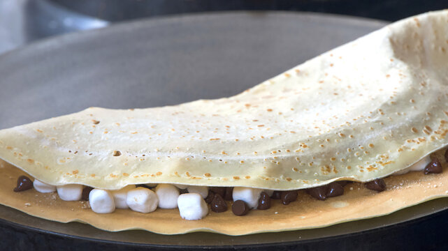 Close up on a french dessert crepe cooking filled with marshmallows and chocolate.
