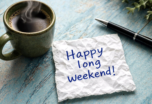 Handwritten happy long weekend message with a hot coffee cup and pen on table