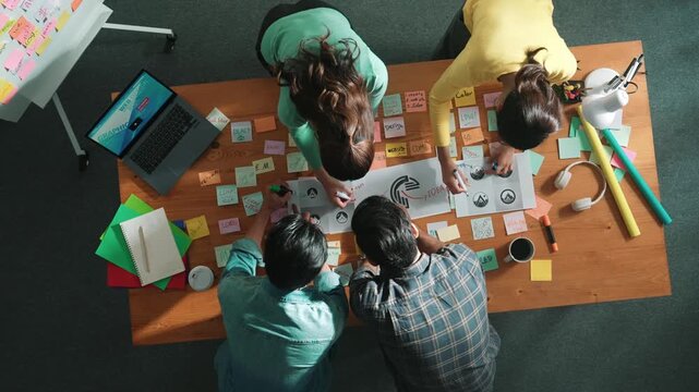 Top view of business team write graphic logo on meeting table with colorful sticky notes and design while explain idea. Project manager sharing idea and explain concept art to smart team. Symposium.