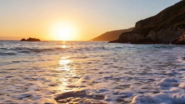 Golden sunset over a serene beach with gentle waves washing ashore and a rocky coastline.