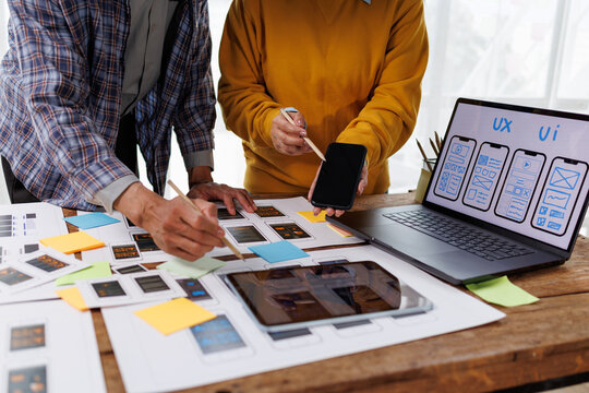 Marketing specialists collaborating on mobile application uiux wireframes and responsive web design, discussing new product development strategies while working with smartphone, tablet, and laptop