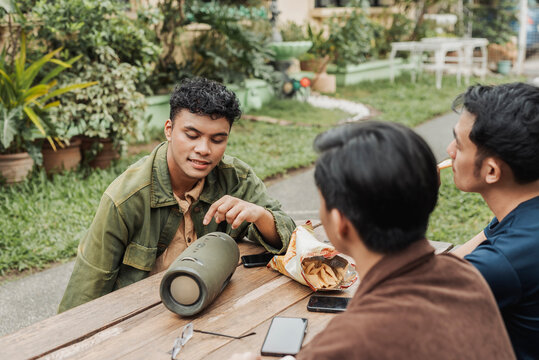 A man explains to his friends about the features of his newly bought wireless speaker. outdoor garden setting.