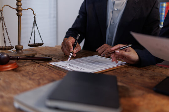 Lawyers or legal professionals discussing a contract document, one signing or illustrating a point on the agreement, representing legal advice, justice, and professional service