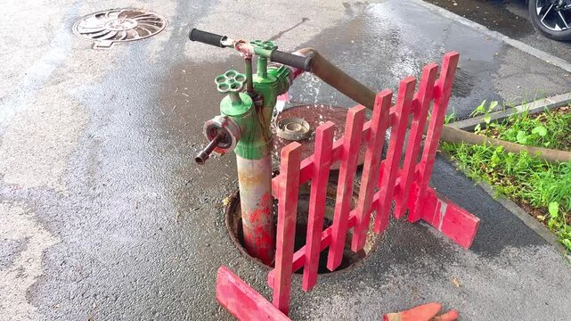 Fire hydrant with red fence and water pooling around it in urban street setting