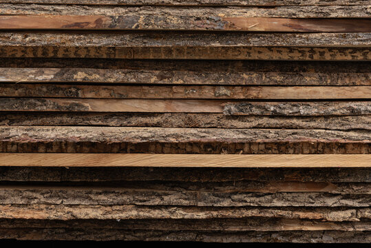 Stacked raw wooden planks with live edge bark background.