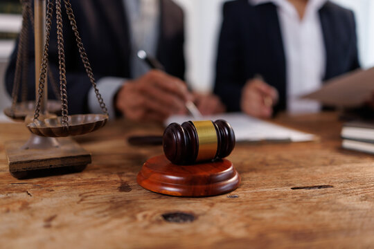 Lawyers engaging in a legal consultation, discussing contract documents with a gavel and scales of justice on the wooden table, symbolizing justice and law